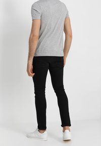 Camiseta gris de manga corta, jeans negros ajustados, zapatillas blancas. Diseño simple con una textura suave, sin patrones ni acentos visibles.