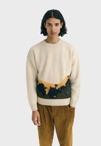 Maglione crema con motivi astratti in verde scuro, giallo e nero nella parte inferiore. Texture lavorata a maglia, collo rotondo, polsini e orlo a costine.
