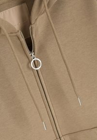 Brązowa bluza z kapturem zapinana na zamek, wykonana z miękkiego materiału. Posiada okrągły metalowy uchwyt zamka i minimalistyczny design. Brak widocznych wzorów lub tekstur.