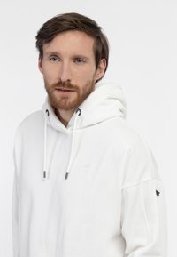 Felpa con cappuccio bianca realizzata in tessuto morbido. Presenta un piccolo logo, cordini con estremità in metallo e una vestibilità leggermente oversize.