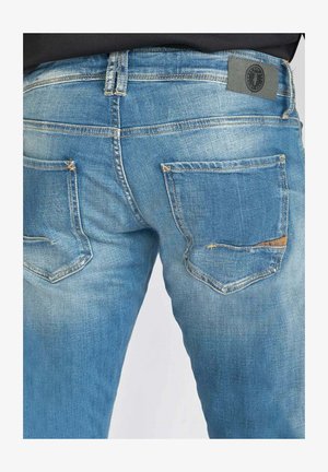 Blauwe spijkerbroek van denim met een licht vervaagde textuur, voorzien van twee achterzakken en een grijs merketiket op de tailleband.