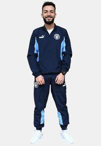 Chándal navy con acentos en azul claro, que cuenta con una chaqueta con cremallera y puños elásticos. Logotipo en el pecho y los pantalones. Deportivas blancas completan el conjunto.