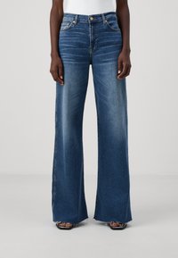 I jeans in denim blu a gamba larga presentano un vita alta, un motivo sbiadito e orli sfrangiati, progettati con cinque tasche e ferramenta in metallo.