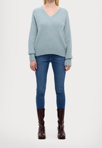 Hellblauer, strukturierter Pullover mit V-Ausschnitt, gerippten Bündchen und Saum, kombiniert mit engen Jeans und dunkelbraunen kniehohen Stiefeln.
