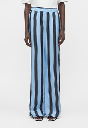 Άτομο που φοράει παντελόνι με ψηλή μέση και φαρδιά μπατζάκια με κάθετες μαύρες και ανοιχτόμπλε ρίγες, σε συνδυασμό με μαύρα πέδιλα με ανοιχτά δάχτυλα και λευκό τοπ.