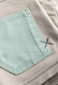 Beige stof met een mintgroene rechthoekige patch met een contrasterend grijze gestikte 'X' detail. Soepele textuur, strakke lijnen.