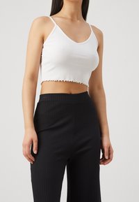 Débardeur court blanc côtelé avec encolure en V et ourlet à volants, associé à un pantalon taille haute noir à rayures fines.