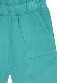 Pantaloni di velluto a costine turchese con cintura elastica e tasca laterale, caratterizzati da una sottile texture a costine.