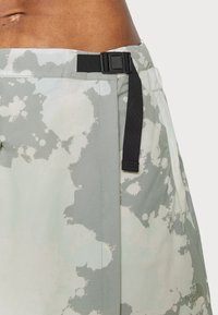 Pantalones cortos ligeros en un verde mate con un patrón abstracto moteado. Presentan un cinturón negro ajustable y bolsillos laterales.