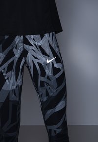 Zwarte en grijze Nike leggings met een abstract geometrisch patroon. Stof is glad met een aansluitende snit en een subtiele logo-accent.