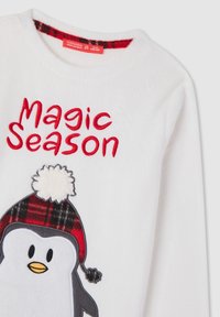 Felpa bianca in pile con un pinguino che indossa un cappello a scacchi rosso e nero. Il testo "Magic Season" è ricamato in rosso.
