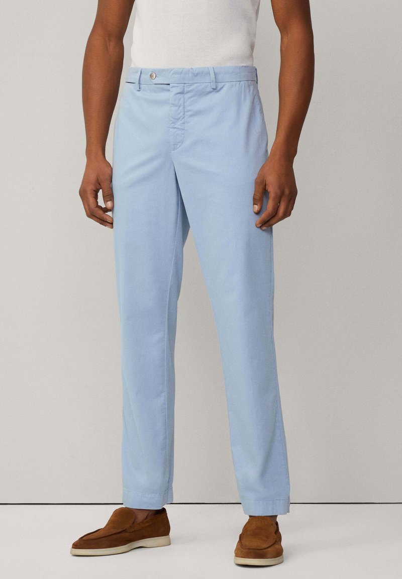 Pantaloni di cotone blu chiaro con taglio dritto, tasche frontali, chiusura a bottone e risvolti, abbinati a mocassini in suede marrone.