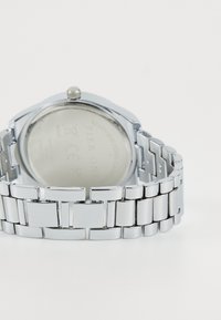 Montre en acier inoxydable argenté avec une finition polie, un boîtier rond et un bracelet à maillons. Présente une couronne visible et un dos lisse.