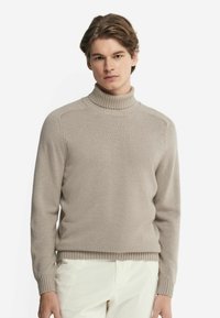 Beige polokrage tröja, tillverkad av mjukt tyg, med ribbad krage och manschetter, har en klassisk passform med minimal detaljering och fin textur.