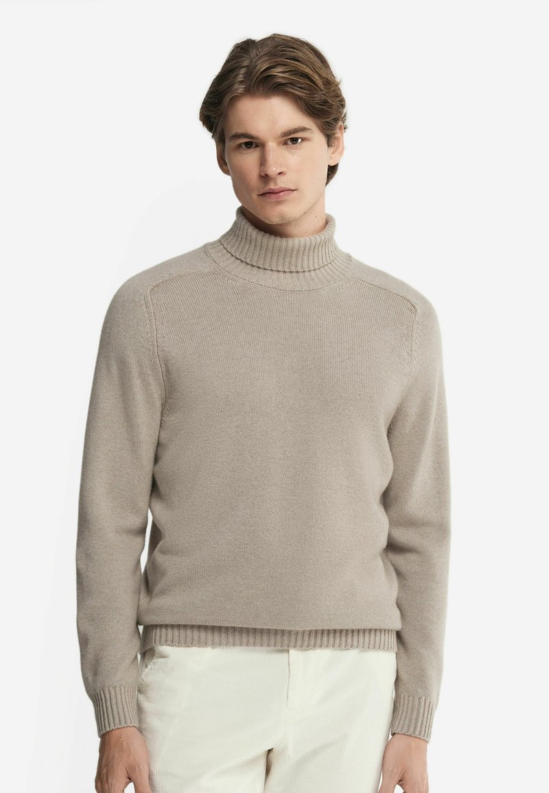 Beige polokrage tröja, tillverkad av mjukt tyg, med ribbad krage och manschetter, har en klassisk passform med minimal detaljering och fin textur.