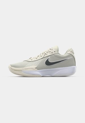 Scarpe da ginnastica beige con tomaia in rete testurizzata, design con lacci, swoosh Nike grigio scuro, suola bianca e marchio "Zoom" sulla intersuola.