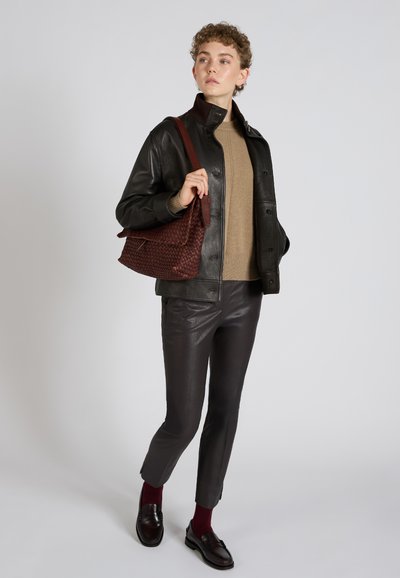 Czarna skórzana kurtka, brązowy dziany sweter, ciemnobrązowe dopasowane spodnie, bordowe skarpetki i mokasyny. Bordowa pleciona torebka dopełnia całość.