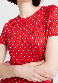 T-shirt rosso con motivo geometrico in bianco e nero. La maglietta ha un collo rotondo e maniche corte, realizzata in tessuto liscio.