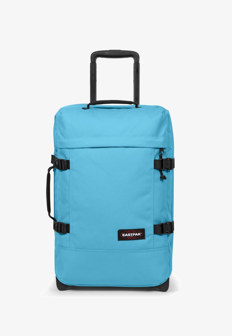 Valigia a rotelle in tessuto azzurro chiaro con manico retrattile, cinghie laterali e frontali, e una patch nera con logo sulla parte anteriore.