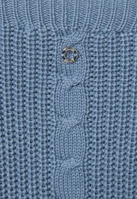 Modrý pletený svetr s texturovaným žebrovaným vzorem, pletenými kabely a stříbrným knoflíkem s rytým logem.