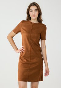 Braunes Kurzarmkleid aus einem samtartigen Material. Figurbetonter Schnitt mit rundem Ausschnitt und seitlichem Schlitz für mehr Bewegungsfreiheit.