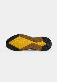 Semelle d’une chaussure Timberland avec un motif de gomme jaune, marron et noir, comprenant des crampons en forme de croix et un petit détail hexagonal vert.