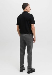 Polo noir associé à un pantalon gris. La chemise a des manches courtes et le pantalon a une coupe slim avec des poches arrière et une texture lisse.