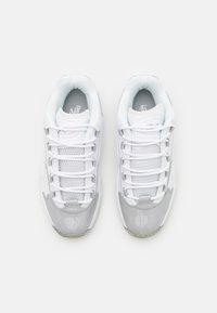 White athletic shoes featuring a glossy grey patent leather toe and a breathable mesh upper with prominent white laces and a padded collar.