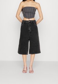 Svart denim culotter med hög midja, bältesöglor och lös passform. Kombineras med en grå strapless topp och rosa sandaletter med remmar.