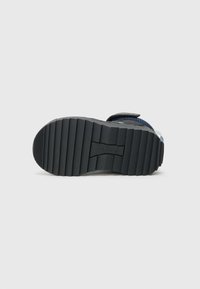 Sola de borracha preta com superfície texturizada e estriada. Parte superior azul com tira ajustável. Apresenta a marca Adidas na sola.