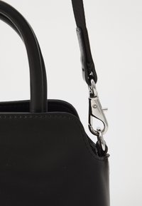 Zwarte leren handtas met een afgeronde vorm. Voorzien van een zilveren metalen clip en een gestructureerde strap die aan de handgreep is bevestigd. Schone stikdetails.