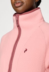 Ροζ φλις μπουφάν με ψηλό γιακά, με φερμουάρ και λεπτομέρειες σε μπορντό χρώμα, που παρουσιάζει υφή και λεπτομέρειες με λογότυπο.