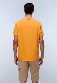 Camiseta amarilla de manga corta con cuello redondo y diseño liso. Combinada con pantalones cortos tipo cargo beige que tienen bolsillos laterales y detalles de botones.