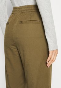 Pantalons ajustés vert olive avec taille élastique, dotés de deux poches arrière et d'un tissu lisse et texturé. Anti-rides avec des jambes droites.