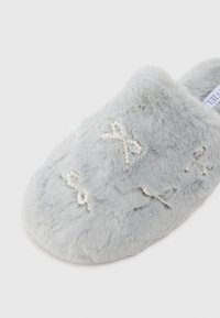 Γκρι φuzzy παντόφλα με απαλό υλικό, διαθέτοντας λεπτομέρειες με χάντρες σε σχήμα φιόγκου και στρογγυλό σχέδιο. Μαλακό και άνετο σχέδιο για χρήση σε εσωτερικούς χώρους.