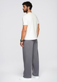 Hvid kortærmet t-shirt parret med løse grå joggingbukser. Bukserne har sidelommer og bæres med hvide sneakers.