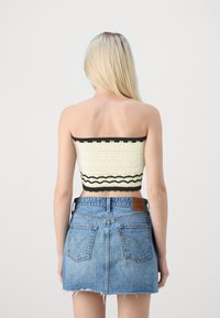 Schwarzes und cremefarbenes gehäkeltes Bandeau-Oberteil mit gewellten Kanten, kombiniert mit einem hellblauen Minirock aus Denim mit fransigem Saum und Gesäßtaschen.