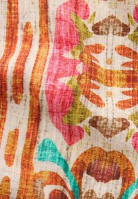 Tissu avec un motif coloré comportant des rayures orange, des formes roses et vertes, ainsi que des éléments floraux sur un fond beige clair.