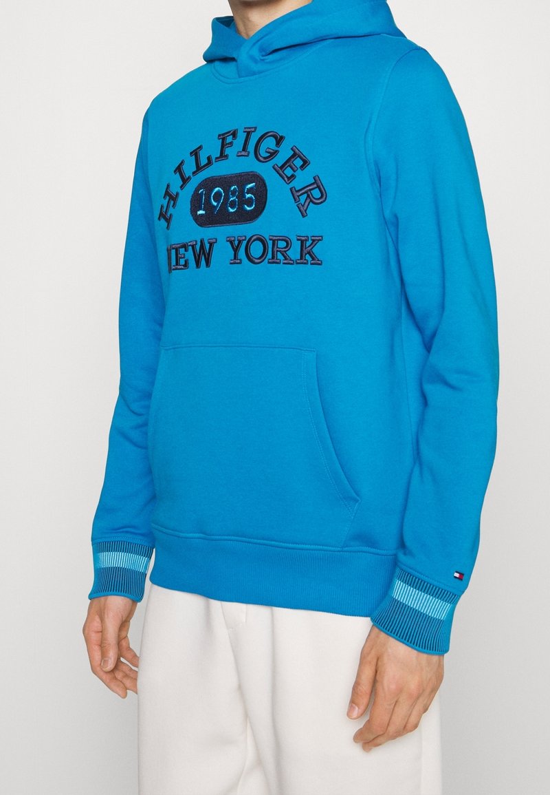 Felpa blu in cotone, con tasca frontale, polsini a costine e logo ricamato "HILFIGER 1985 New York" in nero.