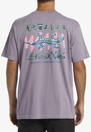 Fioletowa koszulka z krótkim rękawem z kolorowym grafiką gekona na plecach oraz napisem "BILLA BONG ADVENTURE DIVISION" poniżej. Materiał: bawełna.