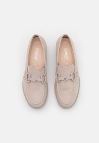 Mocasines de ante beige con una textura suave, que presentan un detalle decorativo de cadena y costuras en contraste a lo largo de la suela.