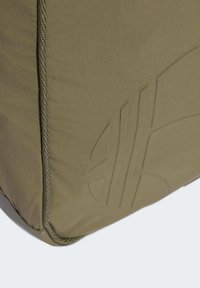 Bolsa retangular verde oliva feita de tecido liso. Apresenta um detalhe de logotipo texturizado e costuras reforçadas nas bordas.