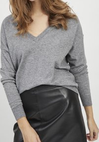 Pull en cachemire gris avec un col en V et des manches longues, associé à une jupe en cuir noir. Les textures contrastent harmonieusement dans la tenue.