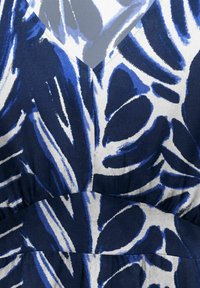 Približan posnetek tkanine z abstraktnim vzorcem listov v mornarsko modri in beli barvi na gubani obleki.