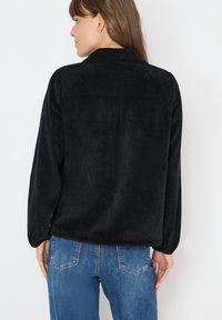 Czarna bluza z polaru o miękkiej fakturze, z kołnierzem i długimi rękawami. Posiada tylną nasadkę i luźny fason. Połączona z niebieskimi dżinsami.