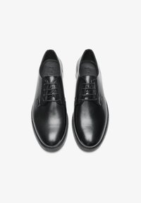 Zapatos de cuero negros con un acabado suave, punta redondeada, diseño de cordones y costuras en contraste alrededor de la suela.