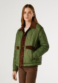 Giacca trapuntata verde con colletto e dettagli in velluto a coste marrone, dotata di due tasche frontali e chiusura con bottoni. Tessuto testurizzato con un aspetto morbido.