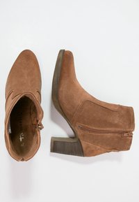 Bruine suède enkellaarsjes met een spitse neus, zijrits en een gestapeld hak. De textuur is zacht met een gladde binnenvoering.