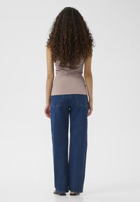 Top a coste marrone chiaro abbinato a jeans in denim blu scuro a vestibilità morbida, visto da dietro, evidenziando la loro forma e vestibilità.