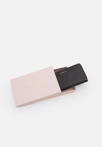 Portafoglio in pelle nera all'interno di una confezione rosa, caratterizzato da una texture granata e il nome del marchio in oro embossato "Coccinelle" sul fronte.